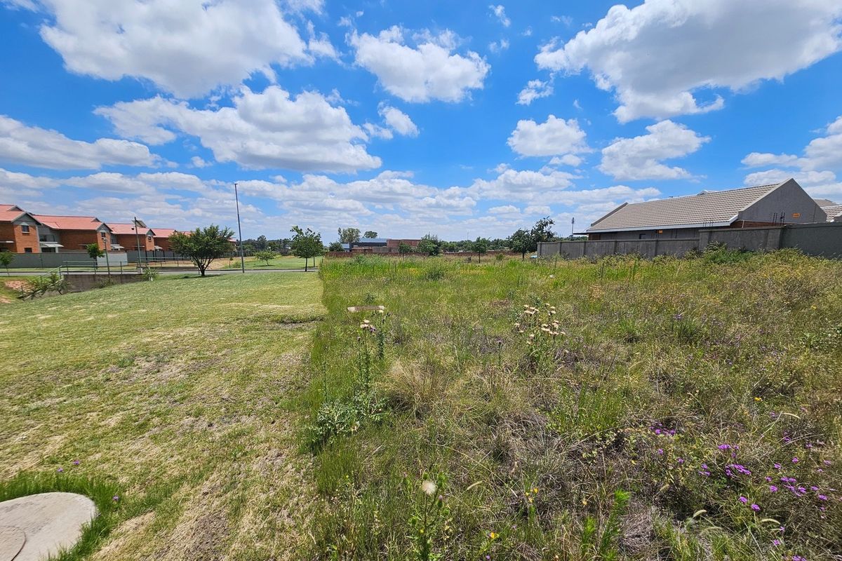 A view of a vacant residential plot featuring natural grassland and surrounding boundary walls in a developed estate setting.