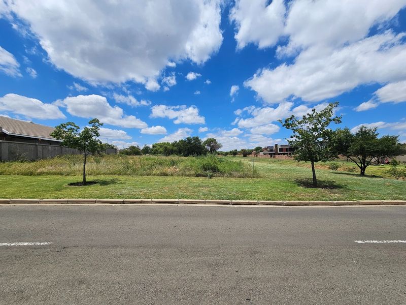 A clear, level residential vacant stand featuring a manicured lawn, young trees, and direct street access in a developed neighborhood.