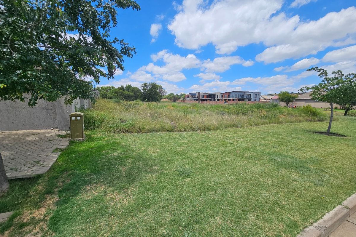 A view of a vacant residential plot featuring a well-maintained lawn, paved walkway, and utility connection point in a suburban estate setting.
