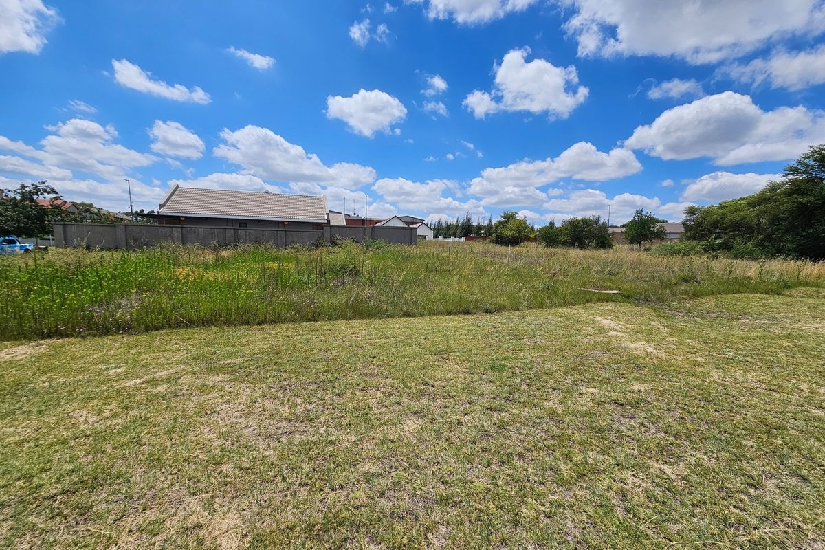 A view of a vacant residential plot featuring a grass lawn and perimeter walling, set against a clear blue sky.