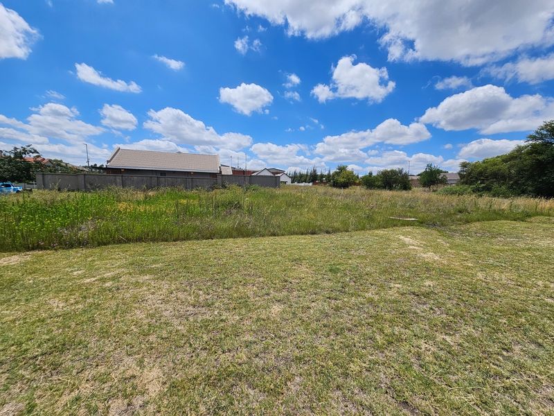 A view of a vacant residential plot featuring a grass lawn and perimeter walling, set against a clear blue sky.