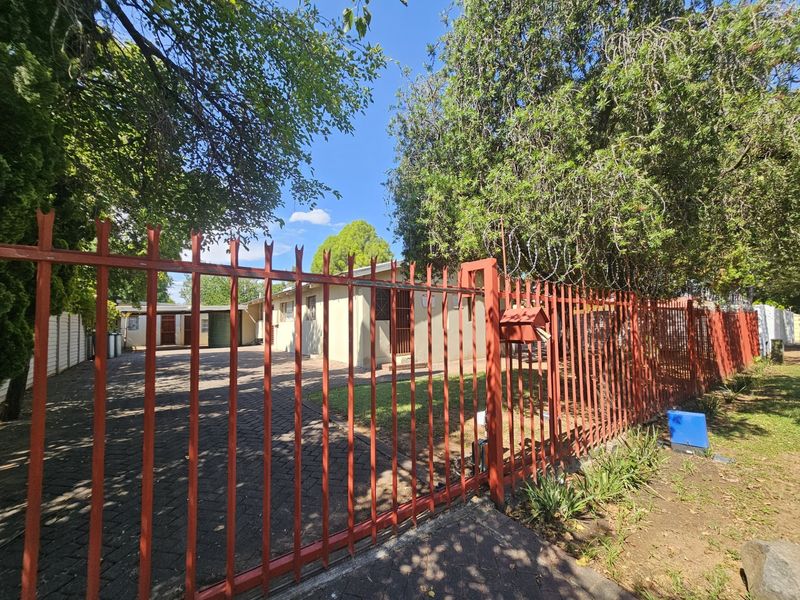 Front view of the property featuring a paved driveway, established garden, and secure steel palisade fencing with razor wire.