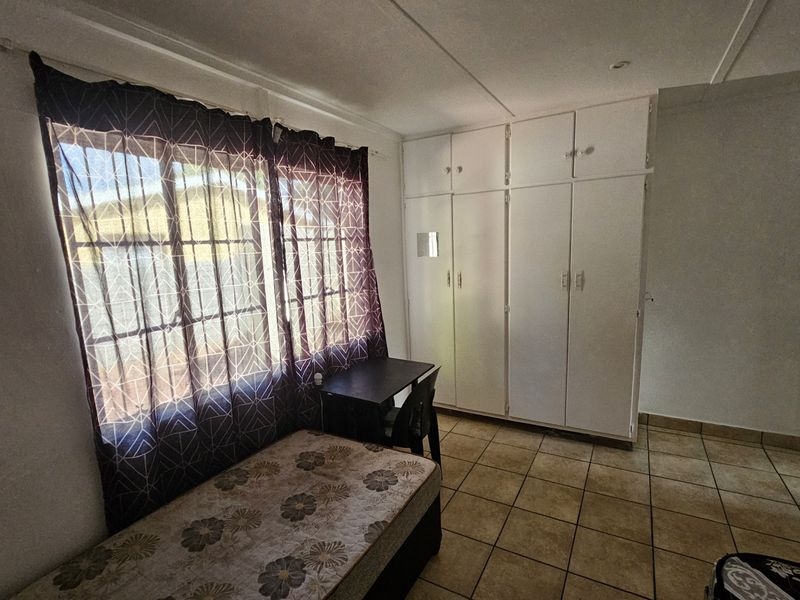 A functional bedroom featuring built-in cupboards, tiled flooring, and a window fitted with security bars for added safety.