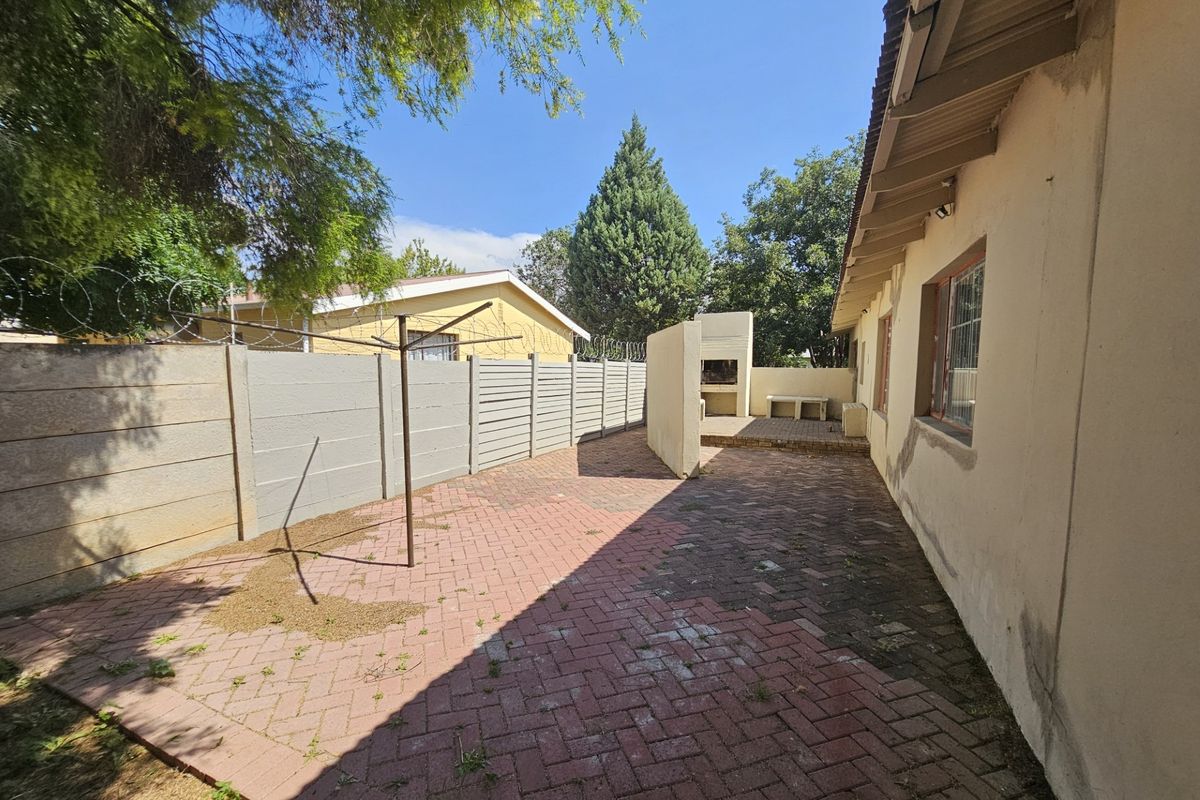 Rear exterior area featuring a paved patio, built-in braai, and perimeter walling with security fencing.