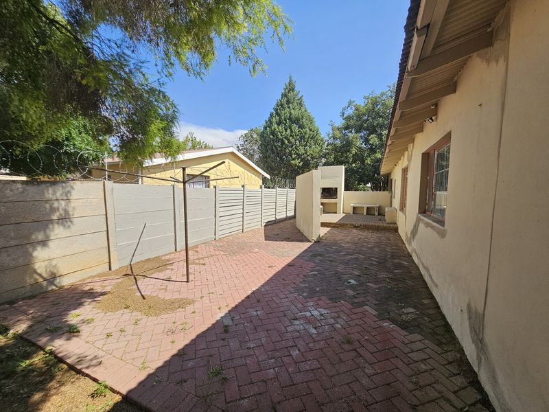 Rear exterior area featuring a paved patio, built-in braai, and perimeter walling with security fencing.