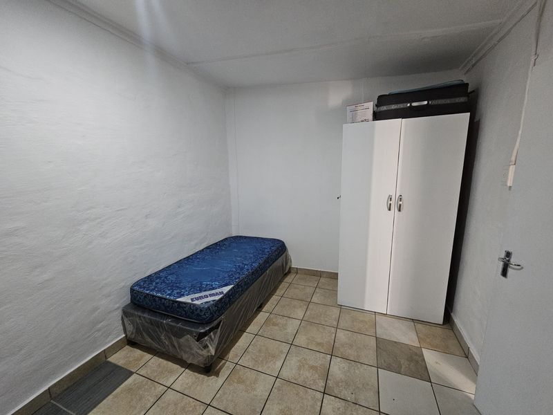 A simple bedroom featuring tiled flooring and a built-in wardrobe, providing a functional and neutral space.