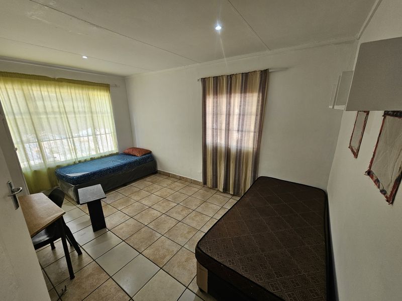 A functional bedroom featuring tiled flooring, recessed downlighting, and dual windows with installed curtain rails.