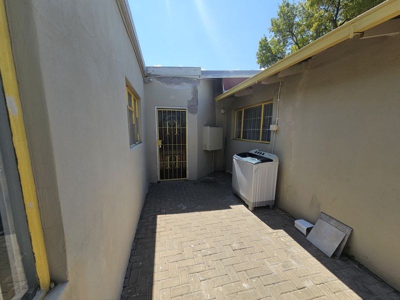 A paved rear courtyard area featuring exterior walls with visible plaster damage and security gate access.