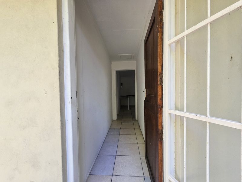 A narrow interior hallway featuring tiled flooring and a timber door, leading towards a secondary utility space.