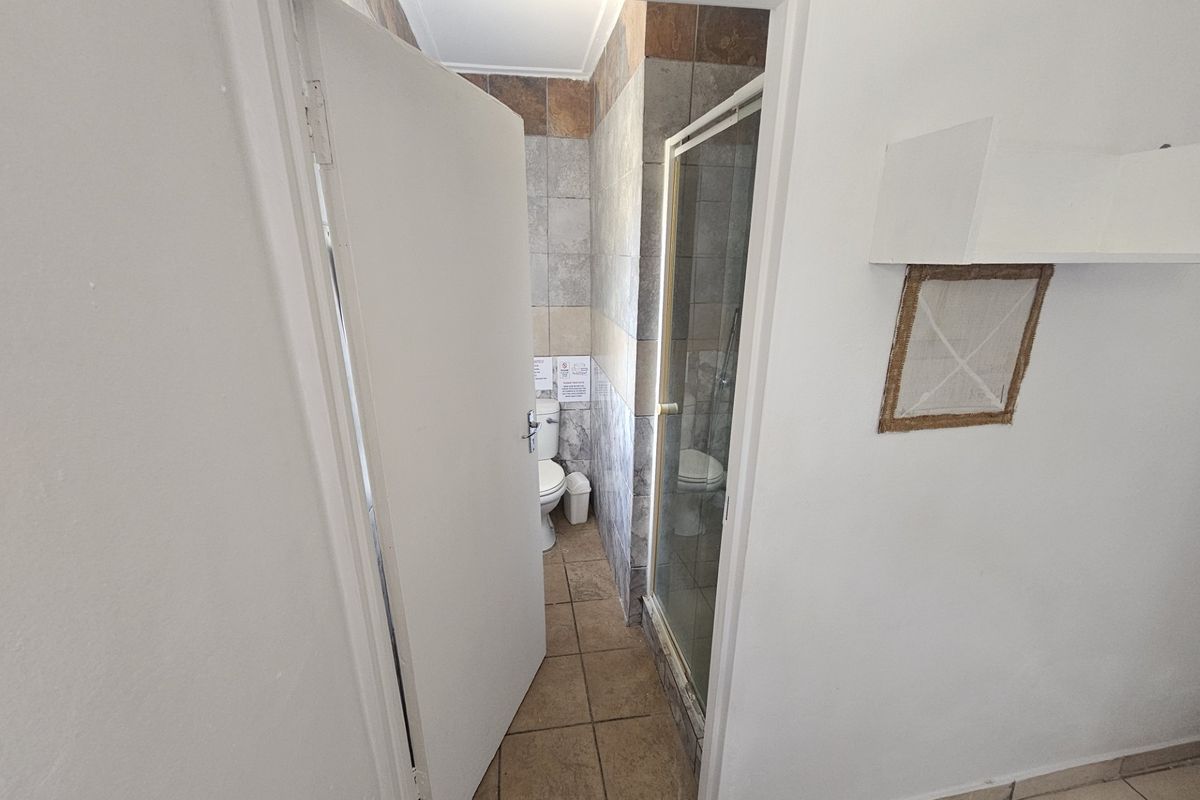 A compact bathroom featuring a shower enclosure and toilet with tiled finishes, accessible via a standard door.