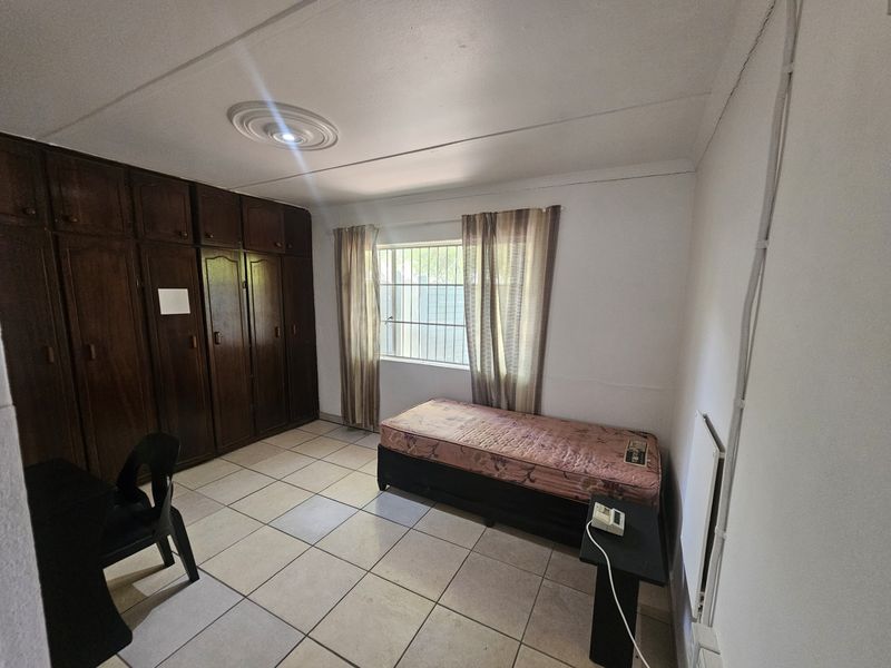 A functional bedroom featuring built-in wooden cupboards, tiled flooring, and security bars on the window.