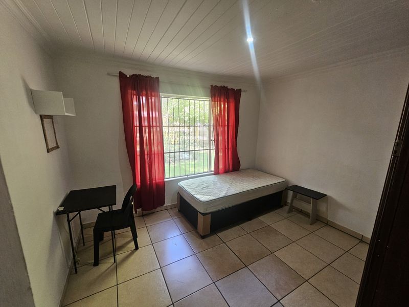 A simple bedroom featuring tiled flooring, security bars on the window, and a tongue and groove ceiling.