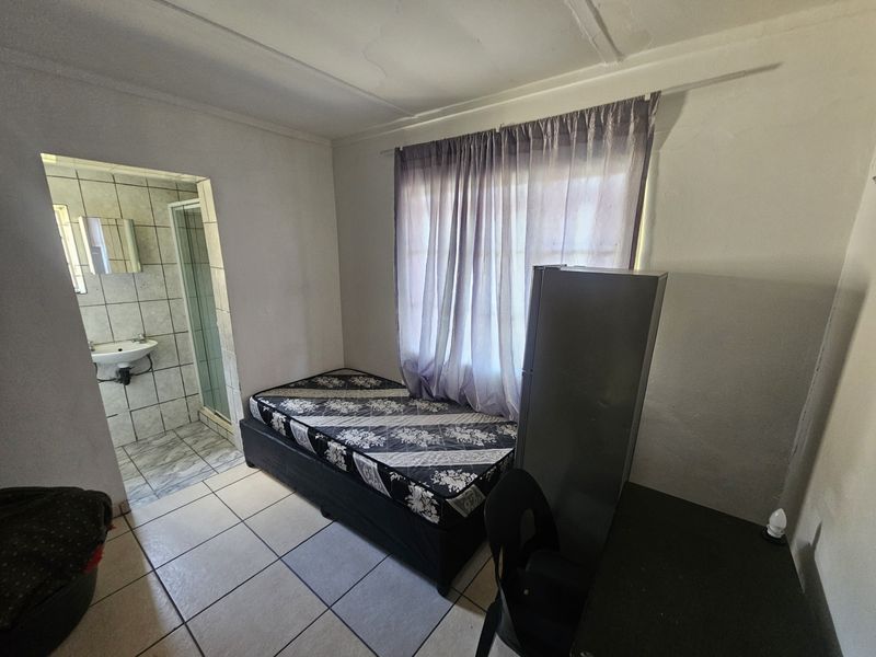 A compact bedroom featuring tiled flooring and an attached en-suite bathroom with shower and basin.