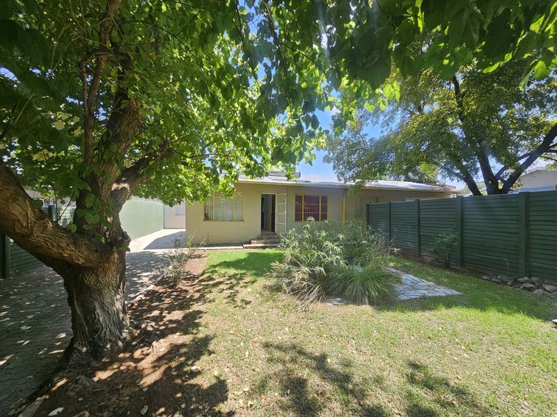 A view of the rear exterior of the house featuring a paved driveway, lawn area, and perimeter timber fencing.