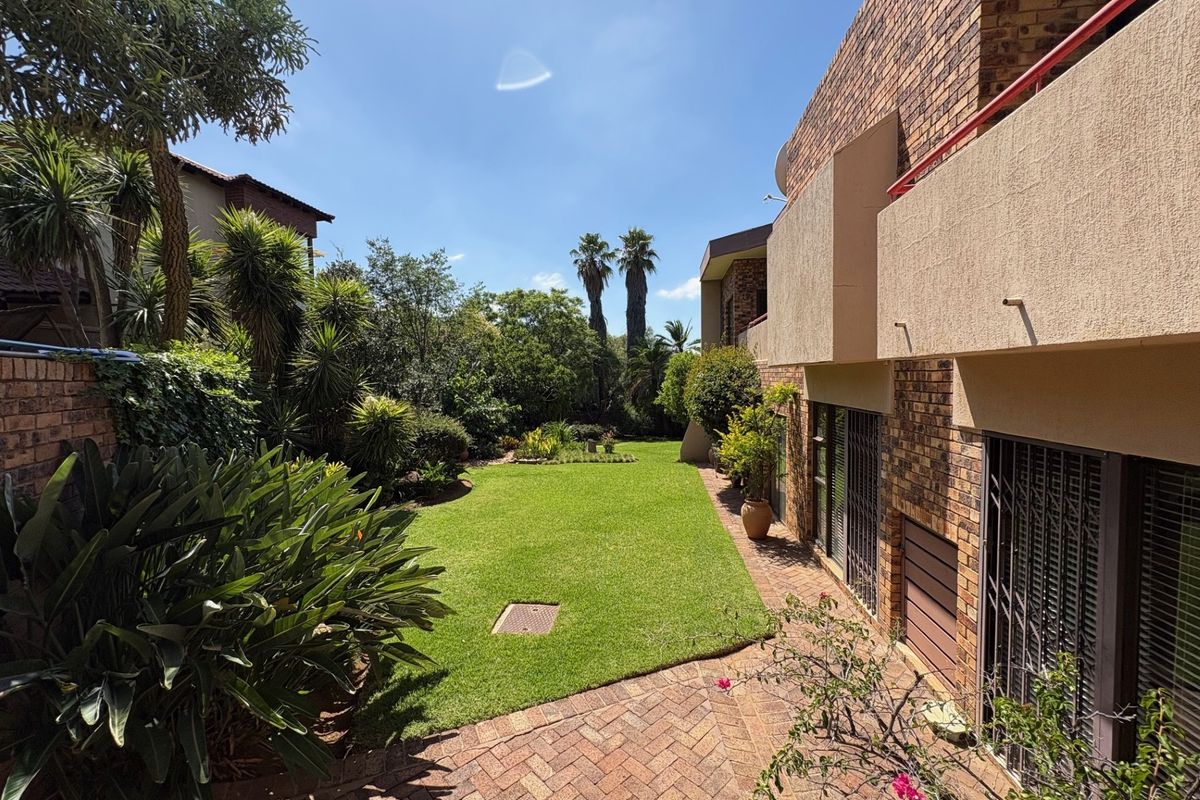 A well-maintained rear garden featuring a lush lawn, established landscaping, and a paved patio area adjacent to the brick-faced residential building.