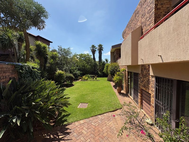 A well-maintained rear garden featuring a lush lawn, established landscaping, and a paved patio area adjacent to the brick-faced residential building.