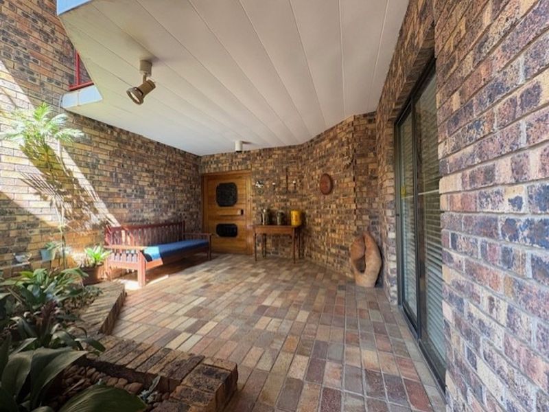 A covered patio area featuring exposed brick walls, brick paved flooring, and a raised brick planter, providing a sheltered outdoor space.