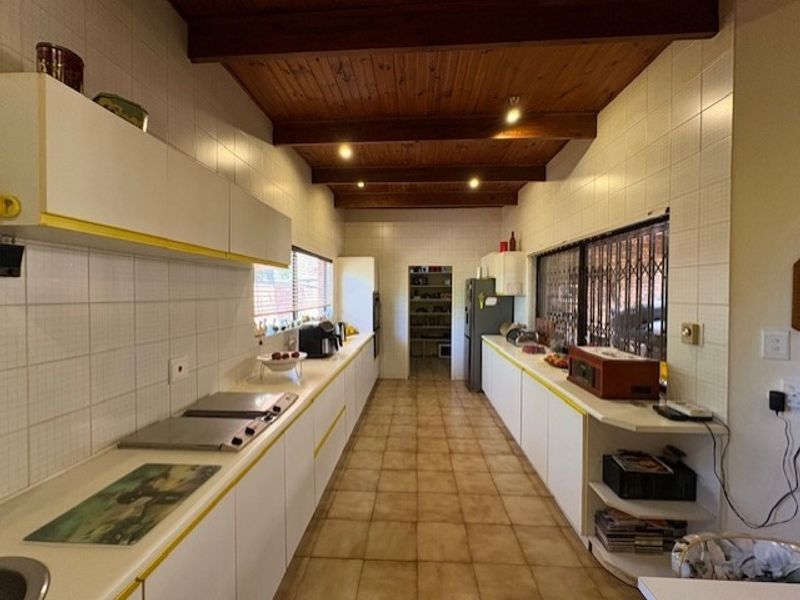 Spacious galley-style kitchen featuring tiled surfaces, ample built-in cabinetry, and exposed timber ceiling beams, offering a functional layout with a separate pantry area.