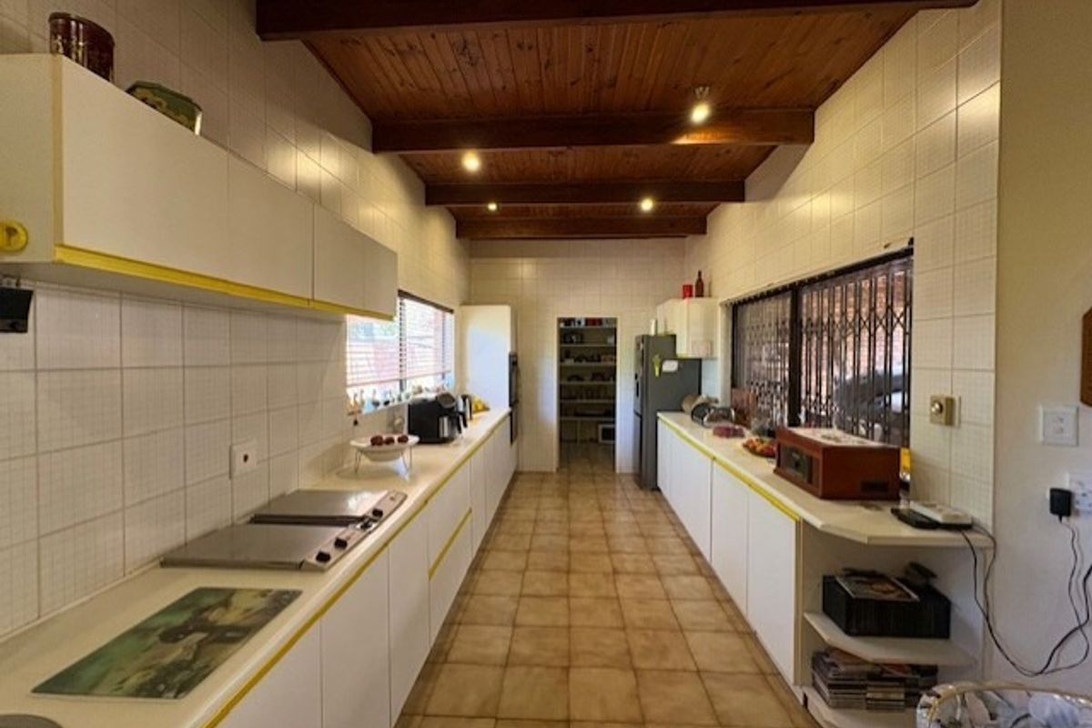 Spacious galley-style kitchen featuring tiled surfaces, ample built-in cabinetry, and exposed timber ceiling beams, offering a functional layout with a separate pantry area.
