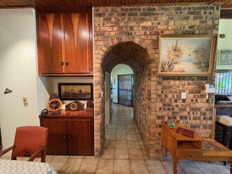 A hallway featuring a distinctive exposed brick archway, built-in wooden cabinetry, and tiled flooring, connecting to an adjacent living space.