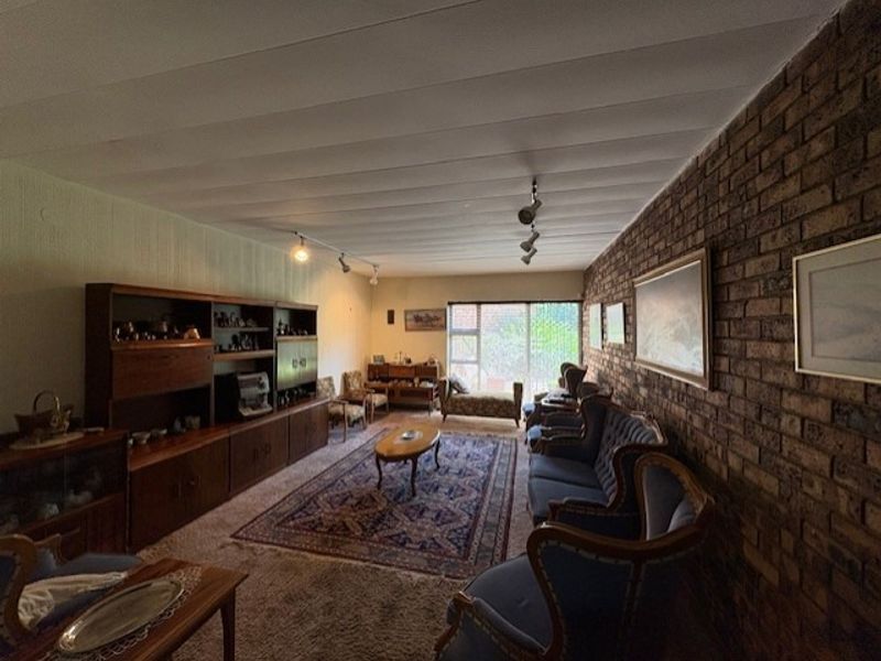 Spacious living room featuring a prominent exposed brick wall, track lighting, and large windows allowing natural light.