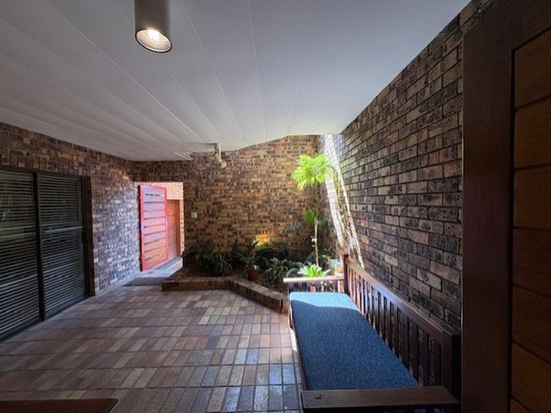 A covered patio area featuring exposed brick walls, tiled flooring, and recessed lighting, providing a sheltered outdoor space.