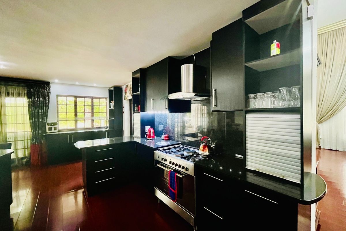 Modern kitchen featuring dark cabinetry, granite countertops, and a stainless steel gas stove with an integrated extractor fan, set against dark laminate flooring.