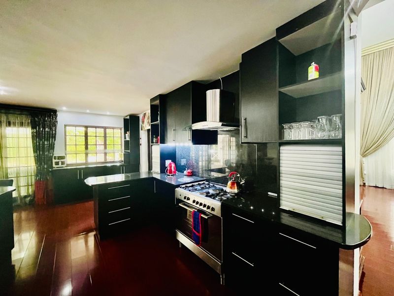 Modern kitchen featuring dark cabinetry, granite countertops, and a stainless steel gas stove with an integrated extractor fan, set against dark laminate flooring.