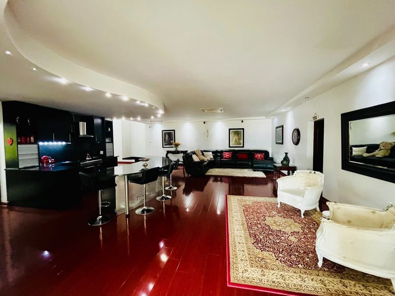 Spacious open-plan living area featuring polished hardwood floors, a modern kitchen with a breakfast island, and a distinctive curved bulkhead ceiling with recessed lighting.