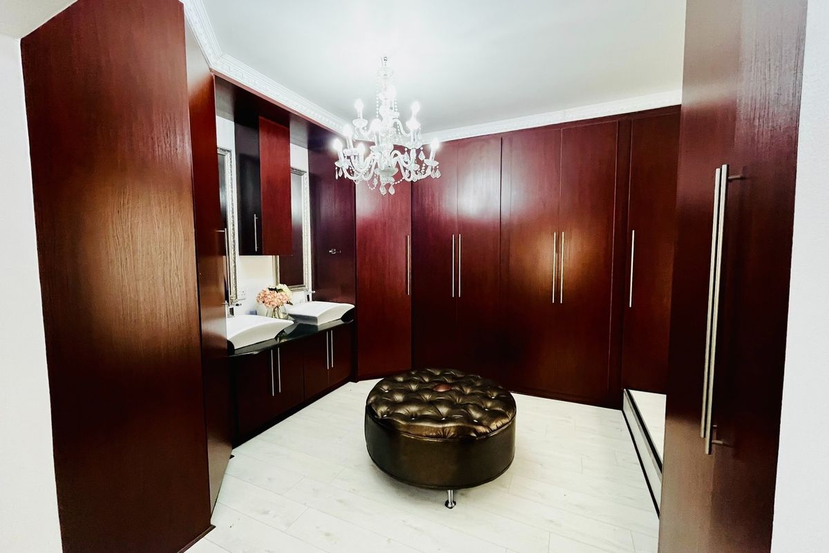 A well-appointed bathroom featuring extensive dark wood built-in cabinetry, dual vessel sinks, and elegant crown molding with a central chandelier.