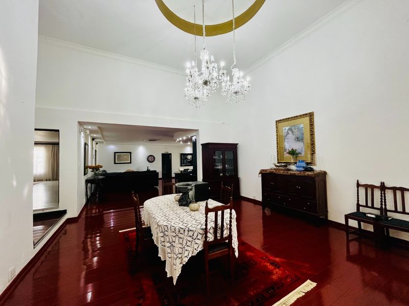 Spacious dining room featuring polished hardwood flooring, high ceilings with a decorative crystal chandelier, and an open-plan flow into the adjacent living area.