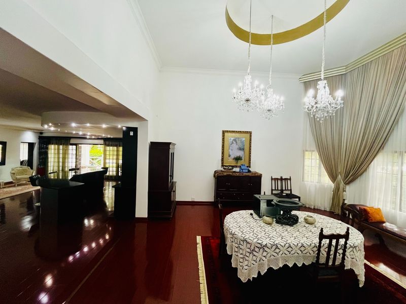 Spacious open-plan living and dining area featuring polished hardwood floors, elegant crystal chandeliers, and high ceilings with decorative cove molding.