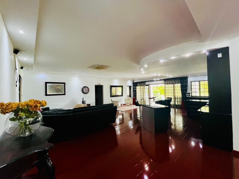 Spacious open-plan living area featuring polished hardwood floors, a coffered ceiling with recessed lighting, and seamless access to the outdoor patio through sliding glass doors.