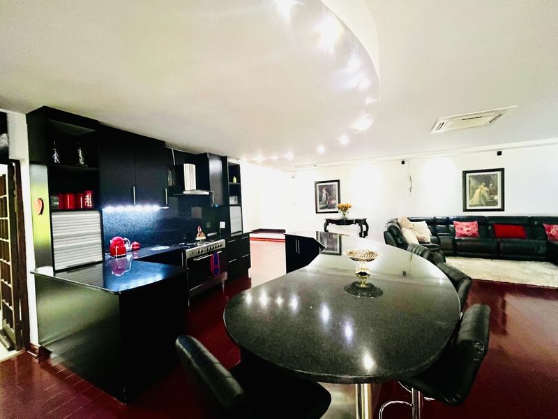Spacious open-plan living area featuring a modern kitchen with black cabinetry, granite countertops, and a large breakfast bar, seamlessly flowing into the lounge.