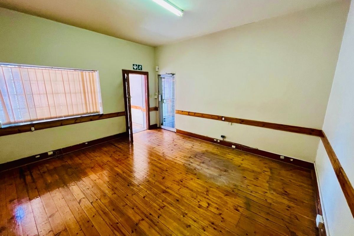 An empty living area featuring original timber flooring, a timber dado rail, and fluorescent lighting, with direct access to an exterior entrance.