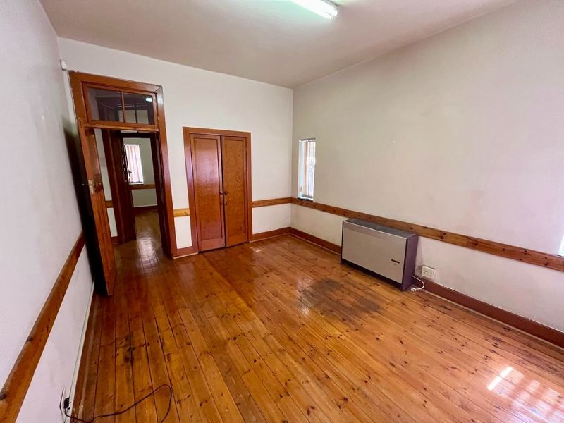 An empty bedroom featuring original timber flooring, wooden door frames, and a dado rail, presenting a dated aesthetic in need of cosmetic updates.