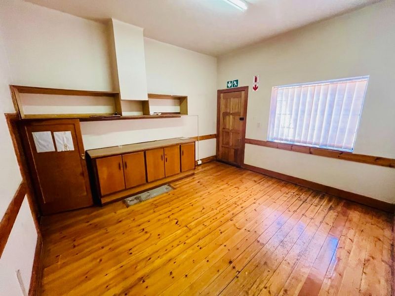 An empty utility room featuring original wooden flooring, built-in wooden cabinetry, and a wooden door, offering a functional space for storage or laundry.