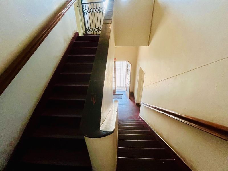 A functional interior staircase and hallway area featuring wooden handrails and security gates, showing signs of wear and requiring cosmetic updates.