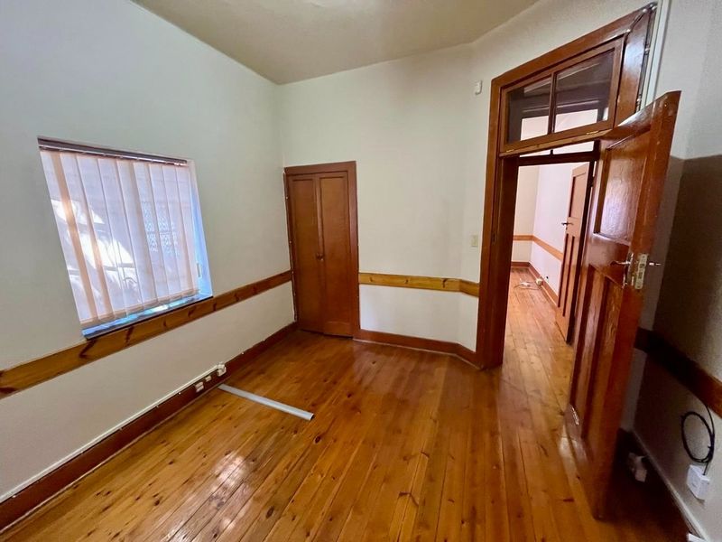 An empty bedroom featuring original timber flooring, wooden door frames, and a built-in cupboard, offering a classic foundation for renovation.