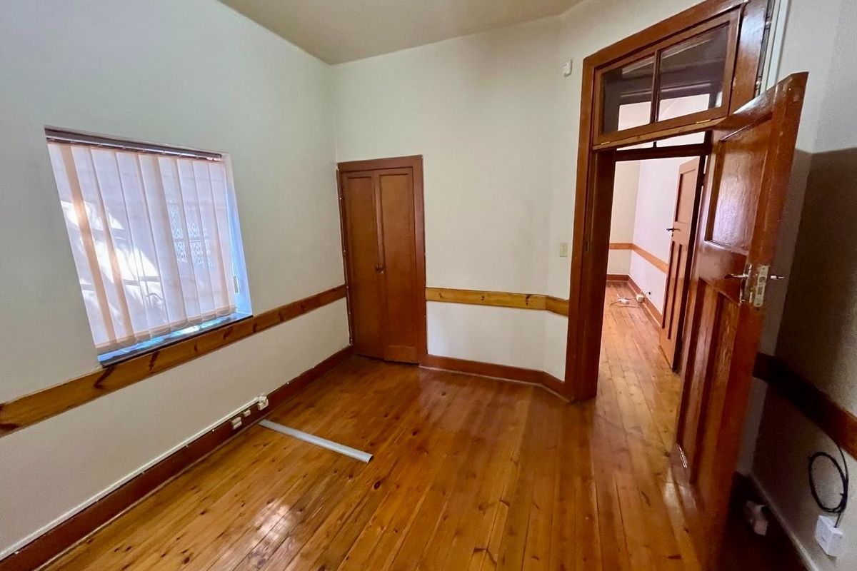 An empty bedroom featuring original timber flooring, wooden door frames, and a built-in cupboard, offering a classic foundation for renovation.