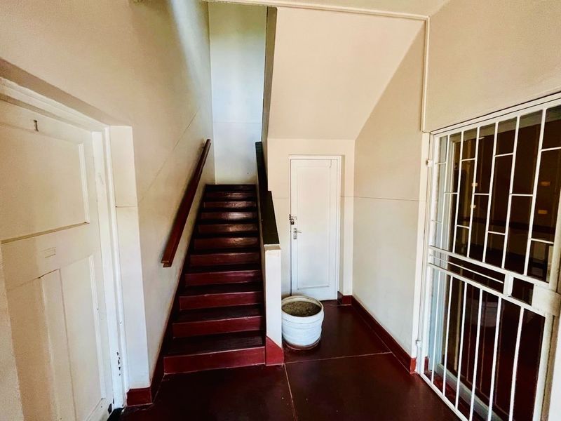An entry area featuring a staircase with a wooden handrail, security gate, and internal doors, showing signs of wear and dated finishes.
