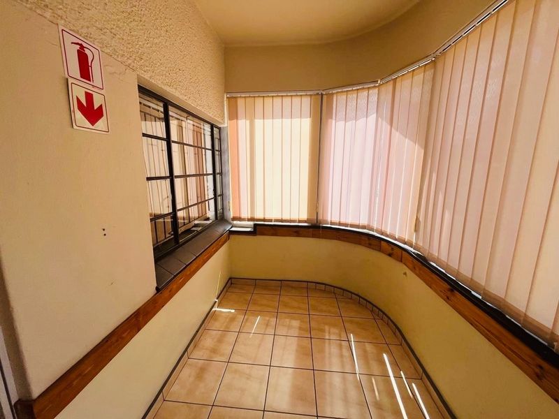 A sunlit enclosed balcony or sunroom featuring tiled flooring, vertical blinds, and security bars, offering a versatile space for relaxation.