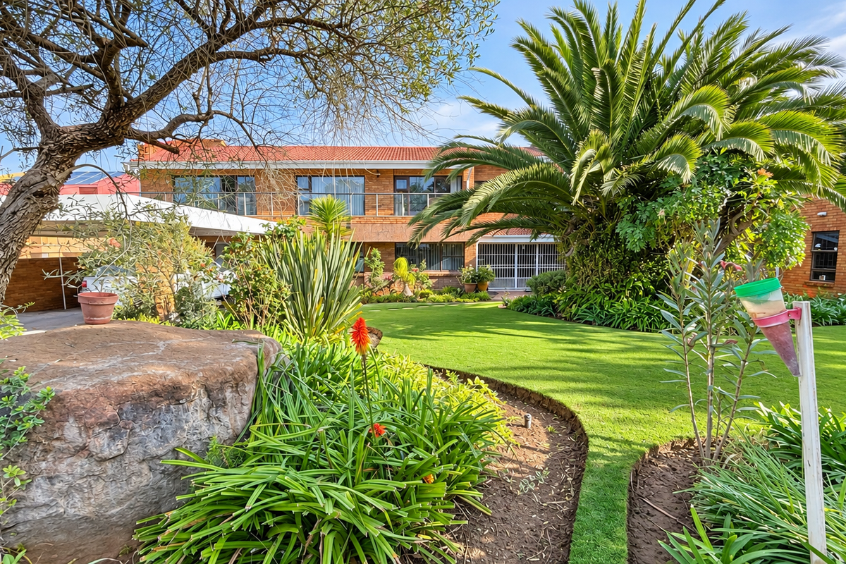 A well-maintained rear garden featuring a lush lawn, mature landscaping, and a brick-faced house with an upper-level balcony.