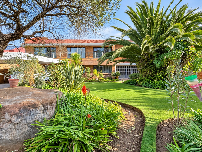 A well-maintained rear garden featuring a lush lawn, mature landscaping, and a brick-faced house with an upper-level balcony.