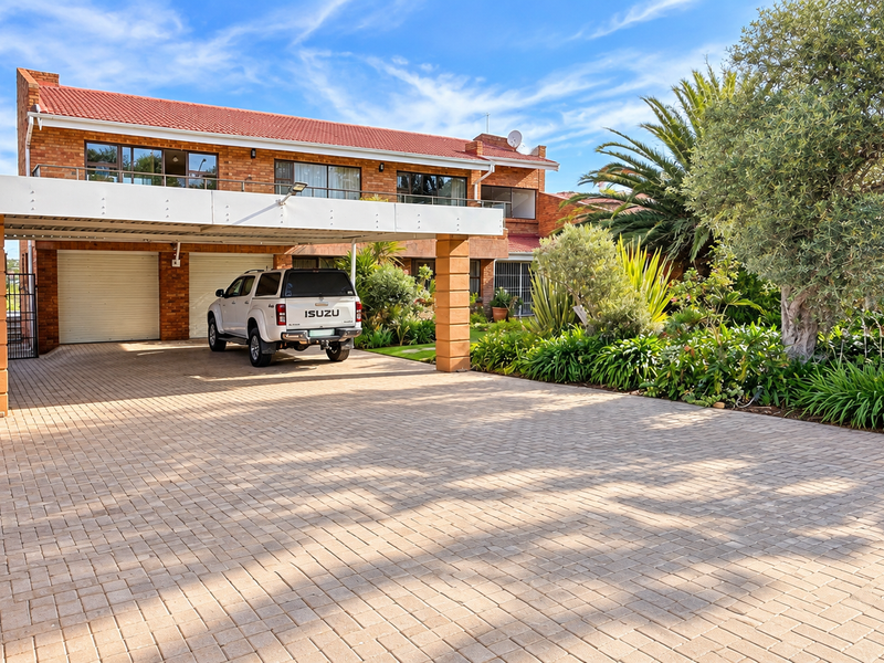 Front view of a double-story brick house featuring a paved driveway, double garage, carport, and well-maintained landscaped garden with electric fencing.