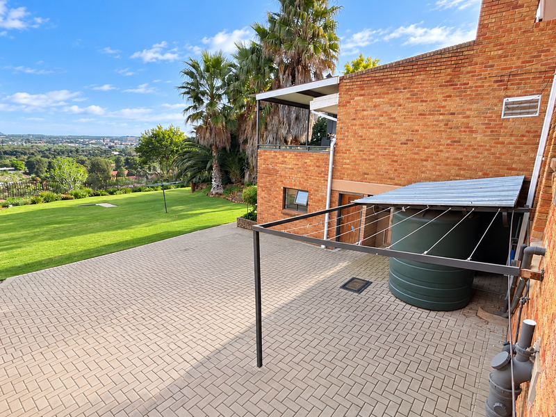 Spacious rear exterior featuring a paved patio, large lawn, water storage tank, and a metal pergola structure against a brick facade.