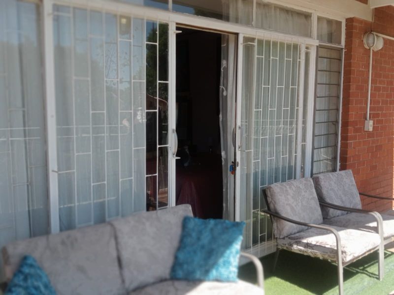 A covered patio area featuring sliding glass doors with security gates, brick wall finish, and integrated outdoor lighting.