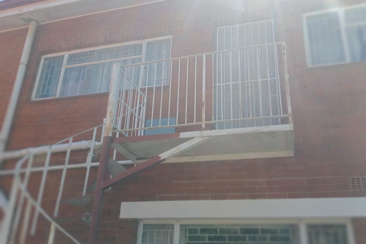 Exterior view of a brick building featuring a metal balcony and an external spiral staircase with visible signs of weathering and corrosion.