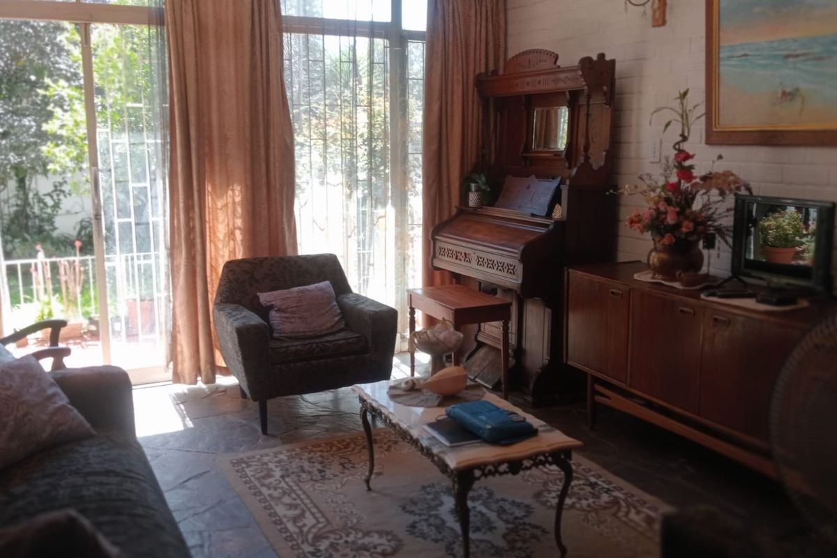 A living room featuring stone flooring, painted brick walls, and large sliding glass doors with security bars providing access to the garden.