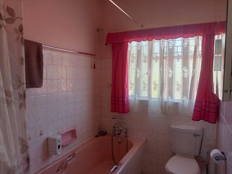 A dated bathroom featuring a pink bathtub, standard toilet, and tiled walls, requiring modernization to improve its aesthetic and functionality.